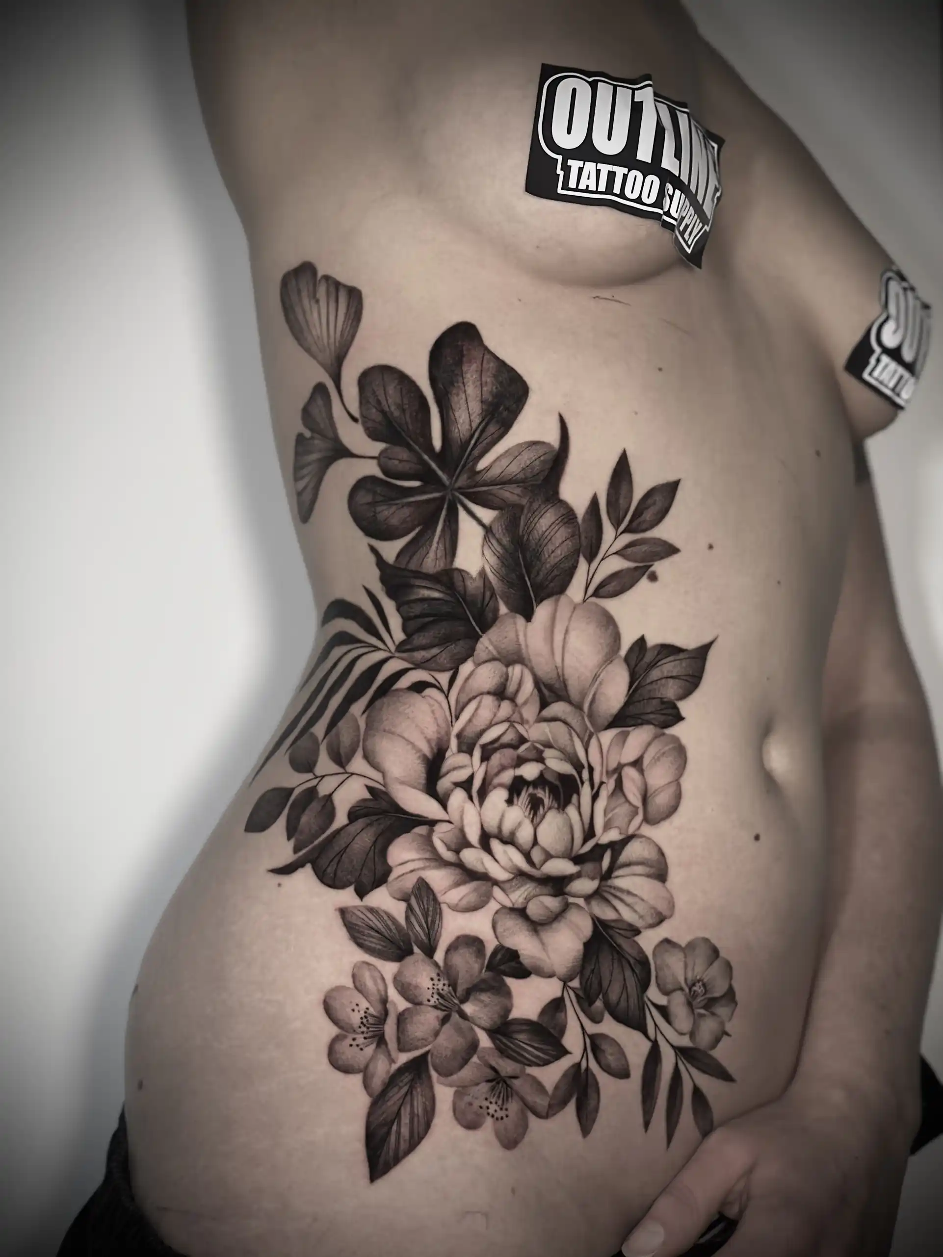 Tatouage floral noir et gris de fleurs sur les côtes — Sainte Elo, Art du Noir Nice